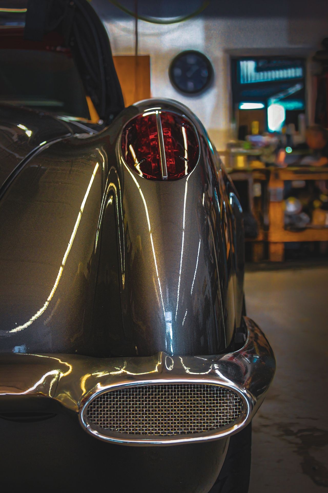 Close-up of vintage car tail light and rear bumper in a garage setting.